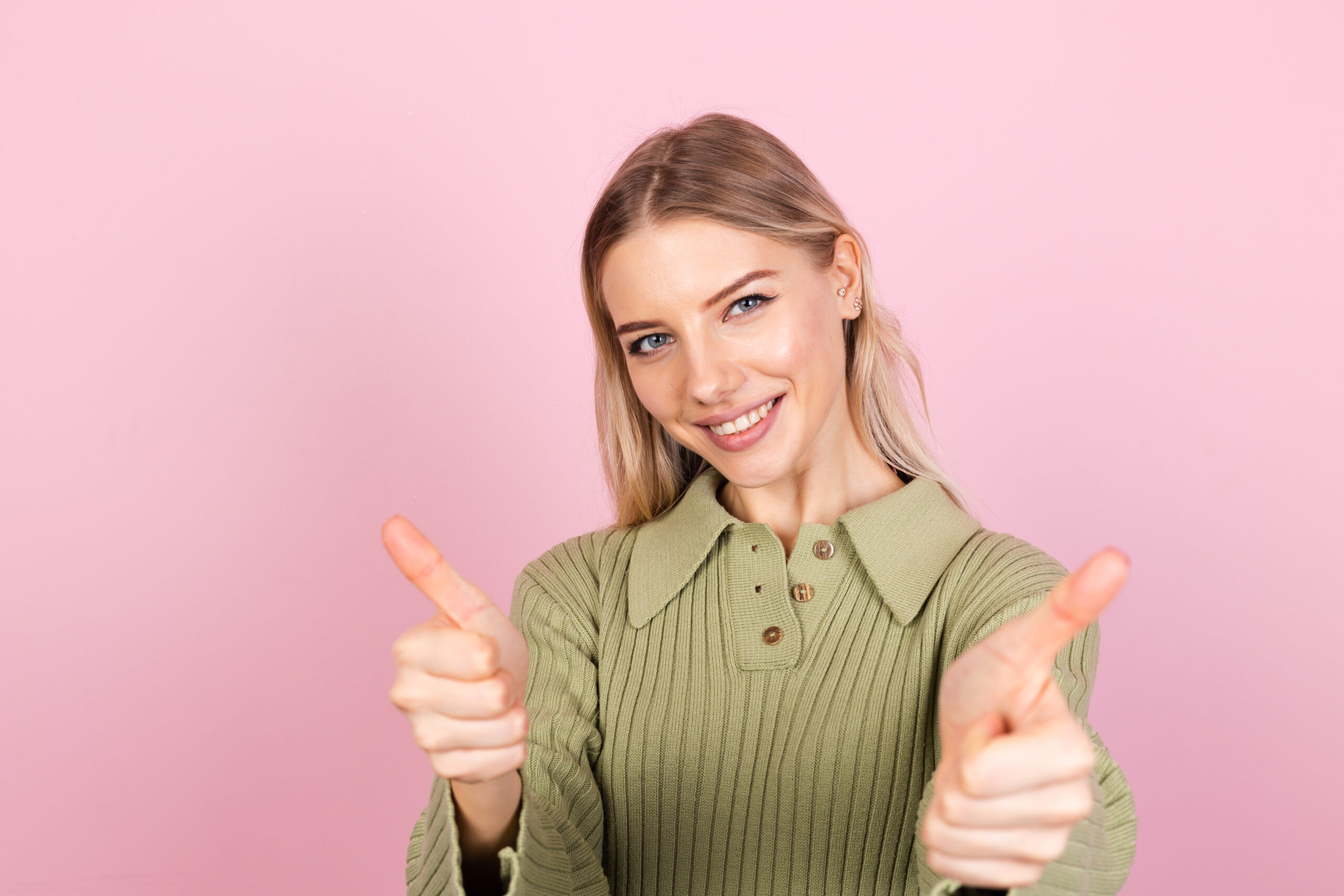 Pretty european woman in casual sweater on pink background happy excited shows thumbs up with big smile